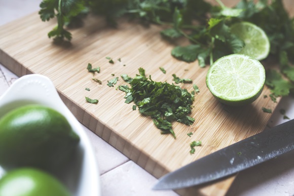 Cilantro and lime being chopped on a wooden chopping board in kitchen